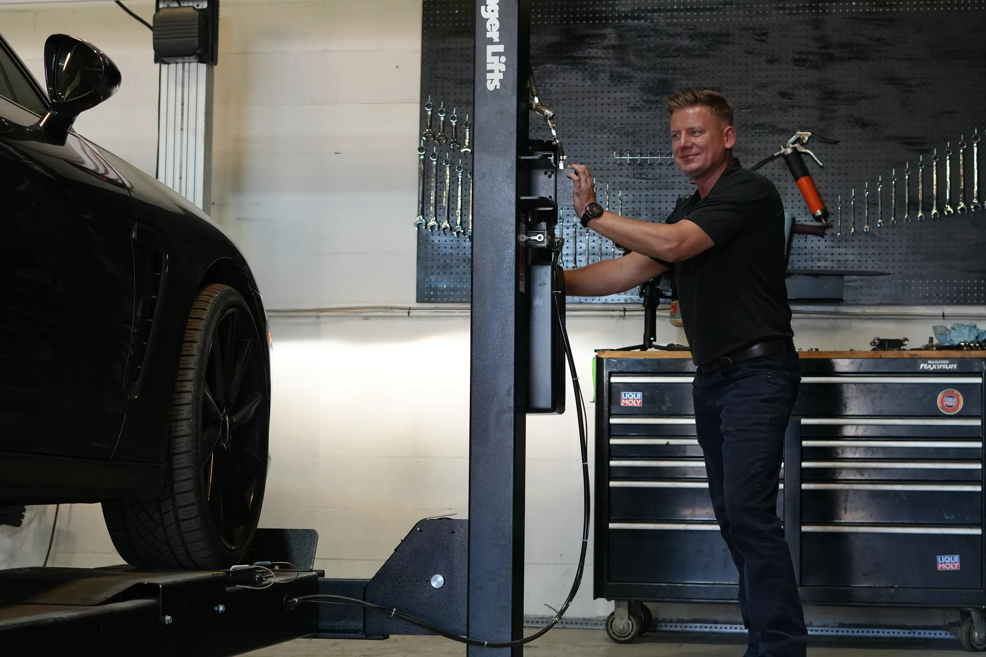 Auto Wise owner operating the vehicle lift beside a car in the workshop.