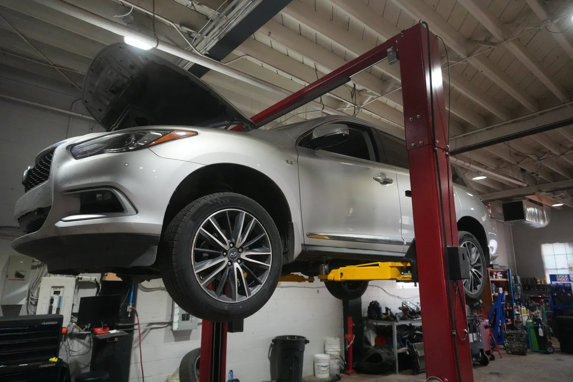 Silver SUV raised on a red service lift with its hood open inside the shop.