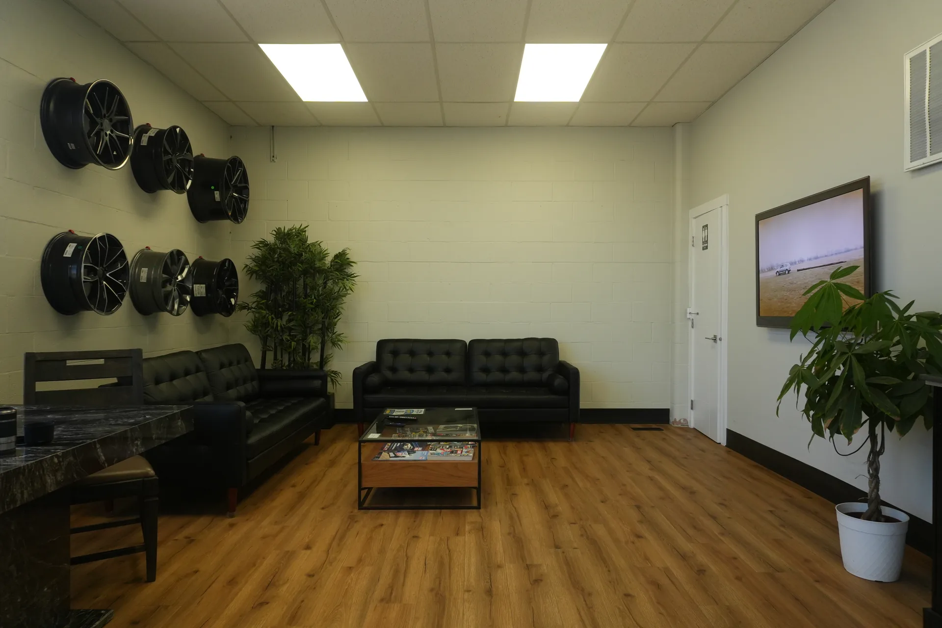 Customer waiting area with black sofas, a coffee table and alloy wheels displayed on the wall.